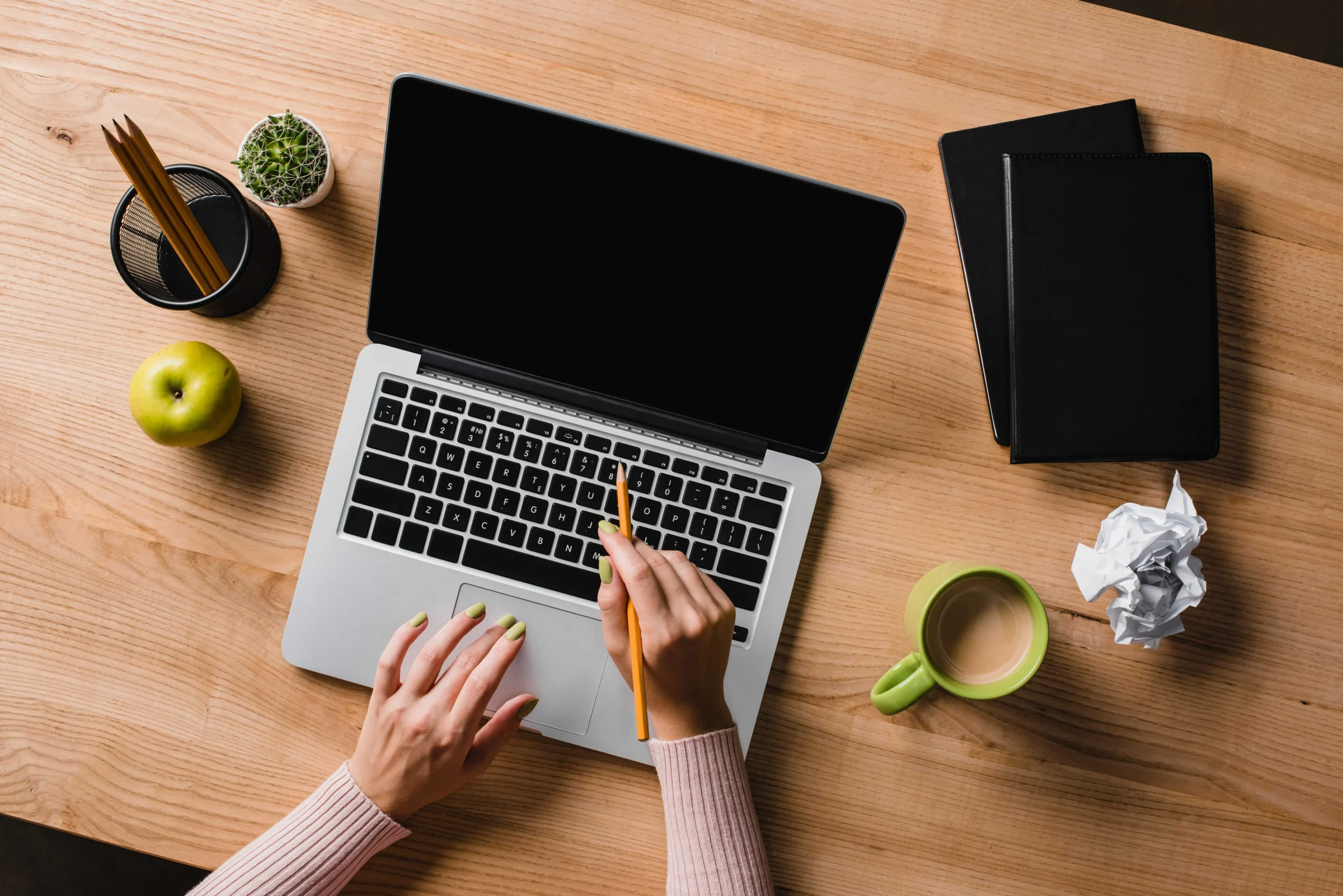 An overhead view of a desk with a laptop, coffee, an apple and crumpled paper.
