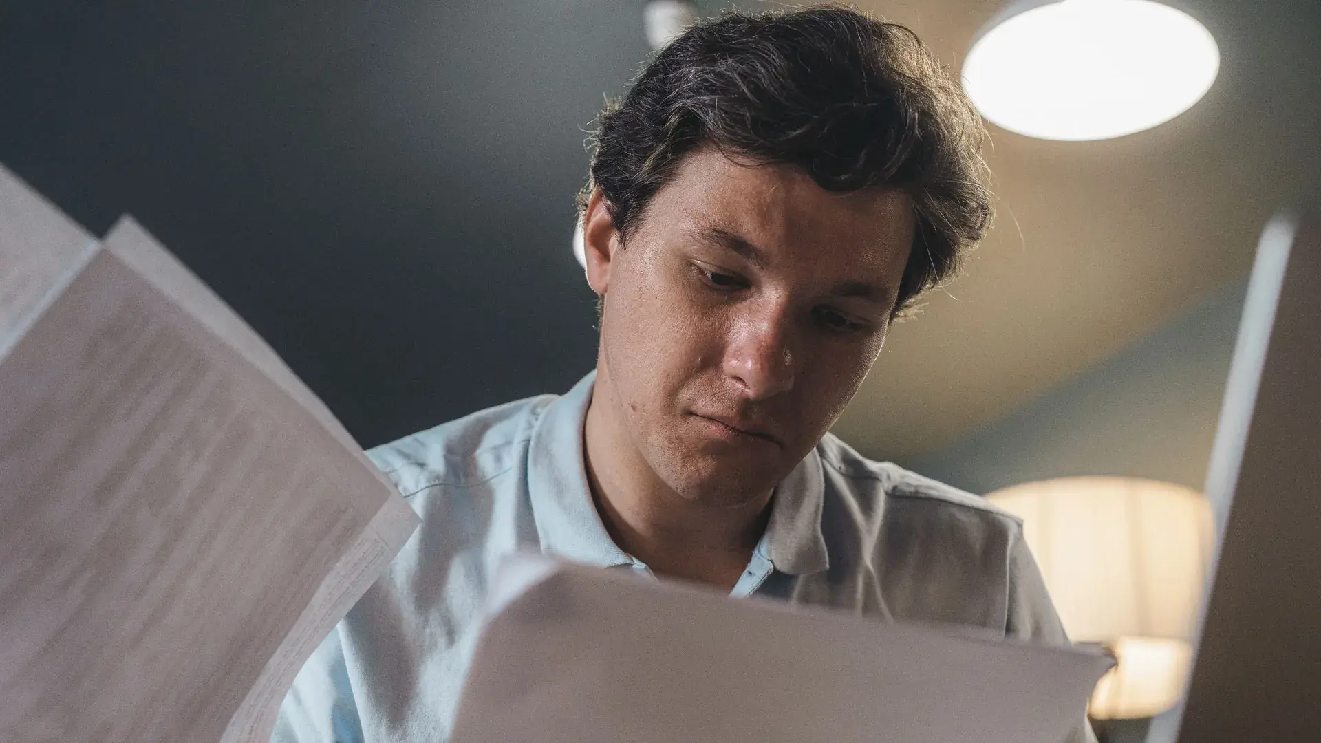 A young man reading printed script pages with a serious expression